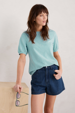 An image of a female model wearing the Seasalt Oleander Blouson Sleeve T-Shirt in the colour Profile Chalk Tidepool.